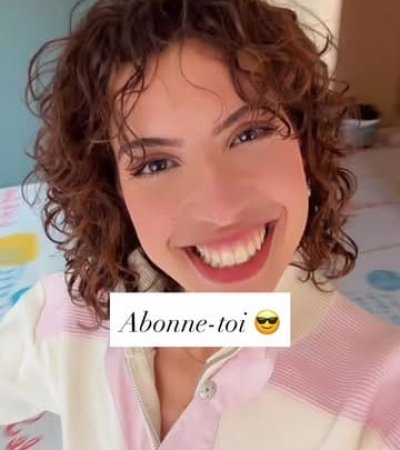 Une jeune femme souriante avec des boucles brunes, encourageant les abonnés.